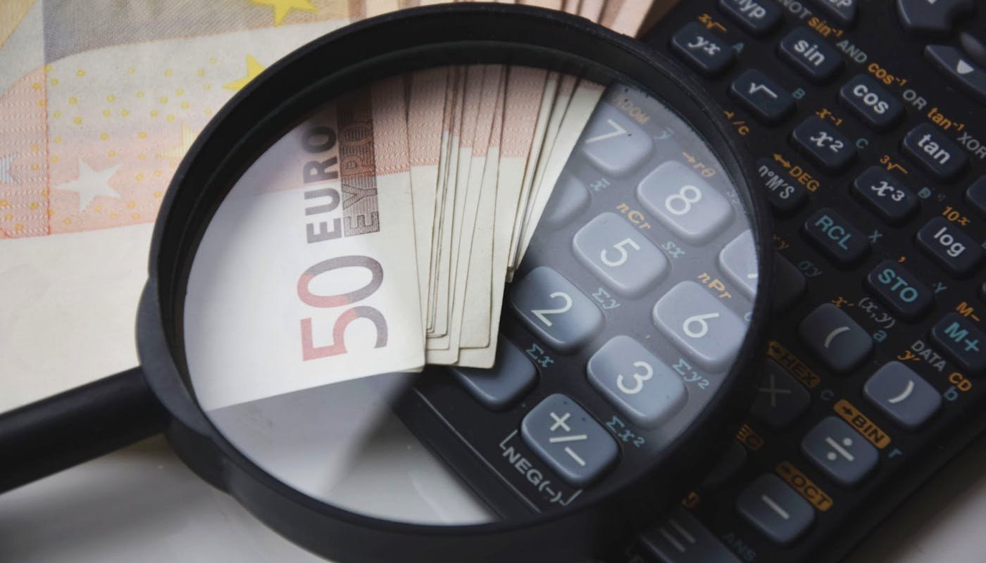 Lupa sobre nota de €50 e calculadora — análisis de cuánto invertir em publicidad para um concesionario de coches usados